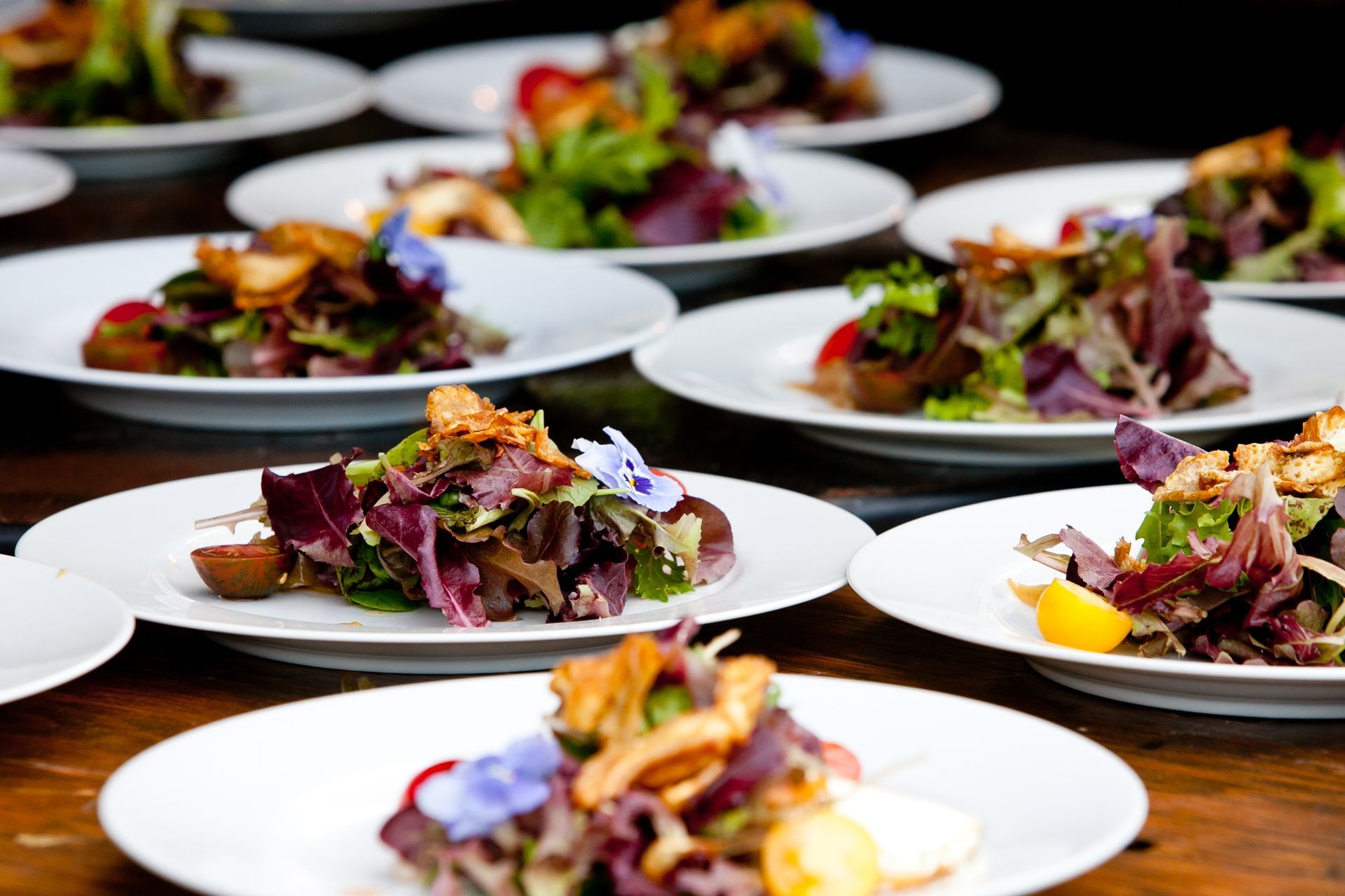 Plates of mixed salad appetizers garnished with purple greens on a wooden table at a catered event