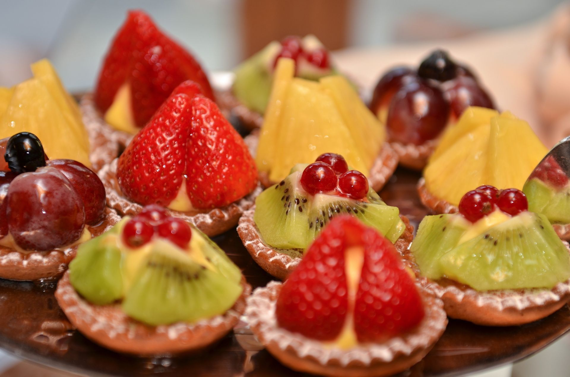 Assorted fruit tarts with strawberries, kiwi, grapes, and orange slices on a wooden tray