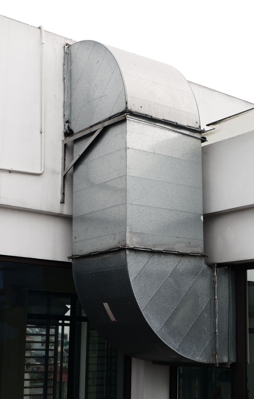 Metal building ventilation duct with a curved section attached to a white industrial wall.
