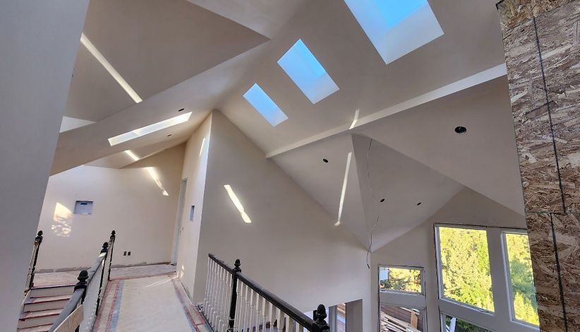Interior view of a modern house with a high, sloped ceiling with skylights. Natural light streams in, illuminating the beige walls and staircase.