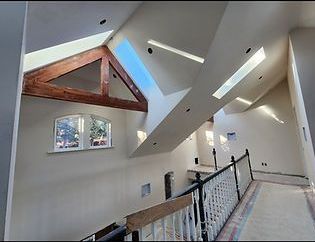 Interior view of a home with a high ceiling, skylights, and a wooden beam. Staircase with a railing is visible.