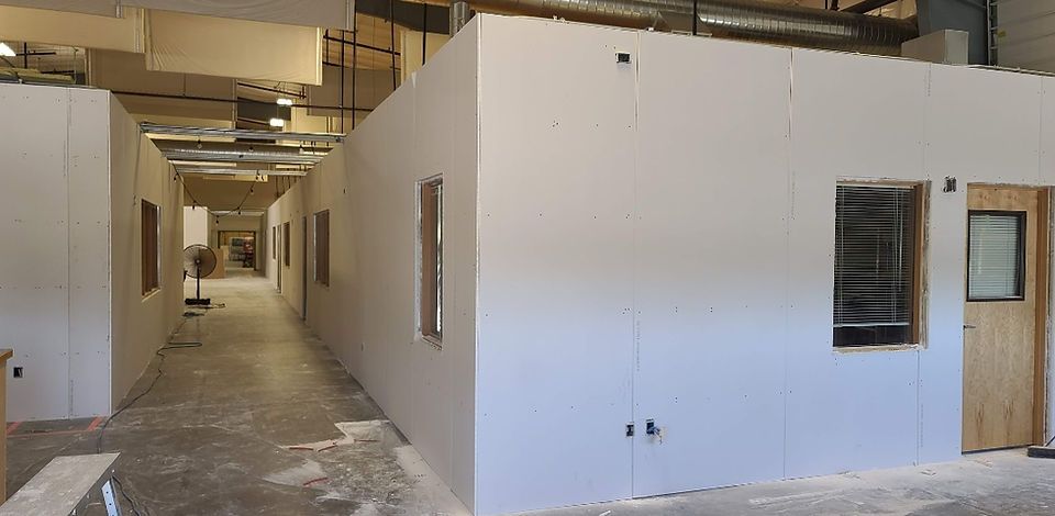 A narrow hallway with white walls and rectangular cutouts for windows under construction. A wooden door is on the right.