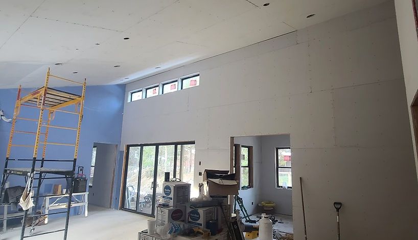 Interior of a room under construction with high ceilings, drywall, windows, a scaffold, and a blue wall.