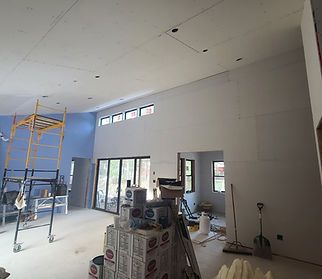 Interior of a house under construction: drywalls, paint cans, scaffolding, large windows and doors.