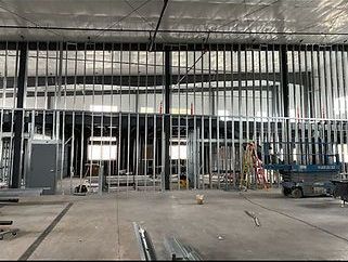Interior construction site with metal stud framing and unfinished concrete floor. A worker and a lift are present.