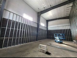 Interior of a steel-framed commercial building under construction. Gray metal studs and insulation line the walls; a blue lift sits inside.