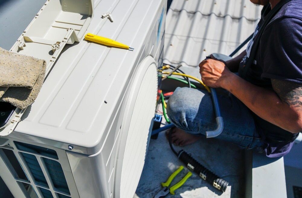 A Man is Sitting on a Roof Fixing an Air Conditioner — Complete Airconditioning & Refrigeration in Darwin, NT