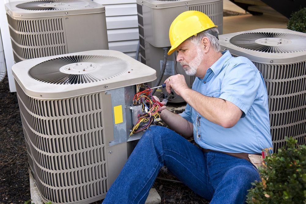 A Man is Sitting on the Ground Working on an Air Conditioner — Complete Airconditioning & Refrigeration in Darwin, NT