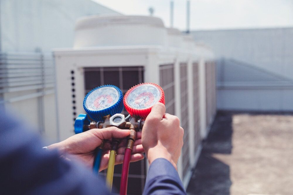 A Man is Holding Two Gauges in Front of an Air Conditioner — Complete Airconditioning & Refrigeration in Darwin, NT