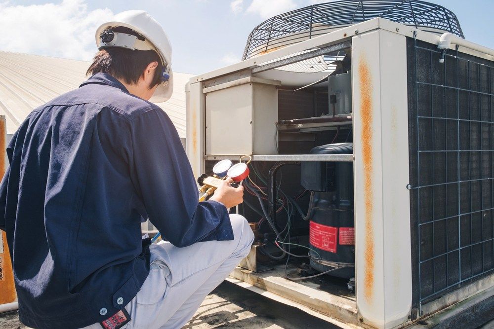 A Man is Working on an Air Conditioner on a Roof — Complete Airconditioning & Refrigeration in Darwin, NT