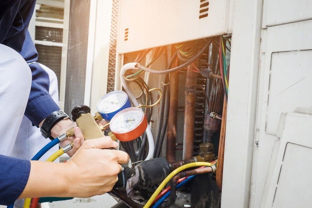 A Man is Working on an Air Conditioner With a Hose — Complete Airconditioning & Refrigeration in Darwin, NT