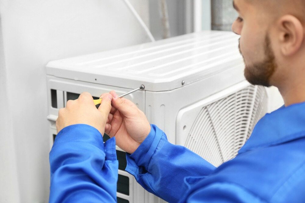 A Man is Fixing an Air Conditioner With a Screwdriver — Complete Airconditioning & Refrigeration in Palmerston, NT
