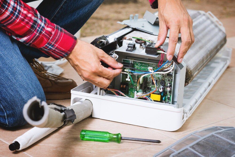 A Man is Repairing an Air Conditioner on the Floor — Complete Airconditioning & Refrigeration in Darwin, NT