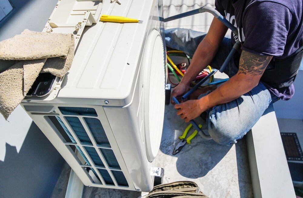 A Man is Working on an Air Conditioner on the Roof of a Building — Complete Airconditioning & Refrigeration in Darwin, NT