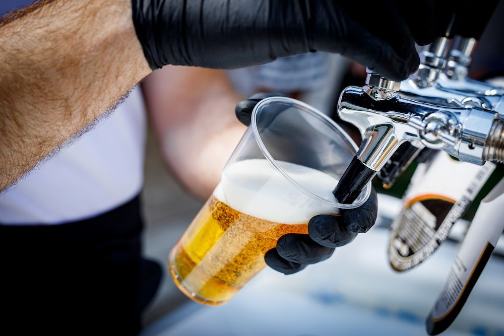 A Person is Pouring Beer Into a Plastic Cup — Complete Airconditioning & Refrigeration in Darwin, NT