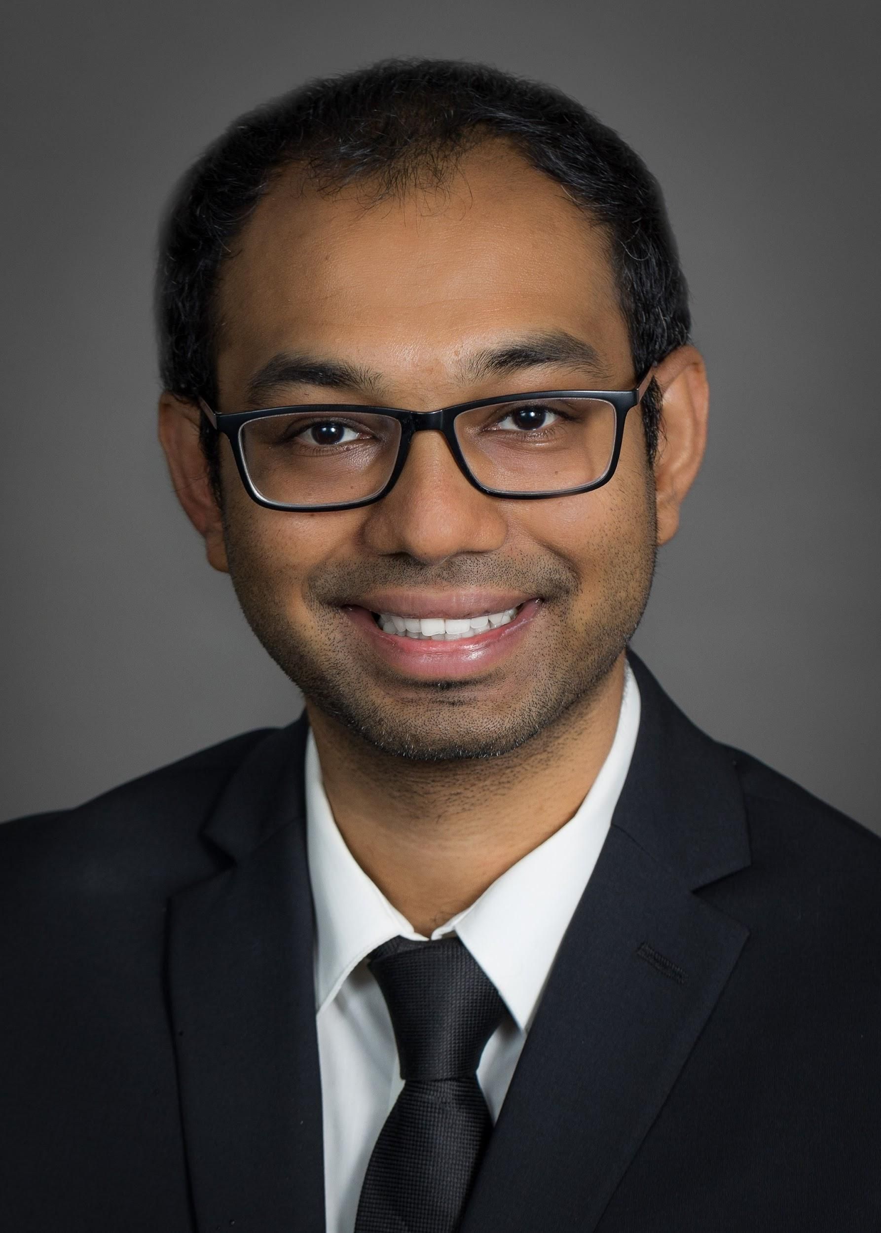 A man wearing glasses and a suit and tie is smiling for the camera.