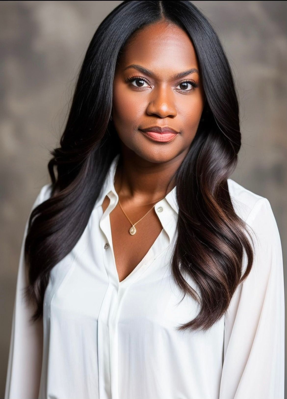 A woman with long dark hair is wearing a white shirt and a necklace.