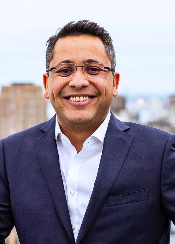 A man in a suit and white shirt is smiling for the camera.
