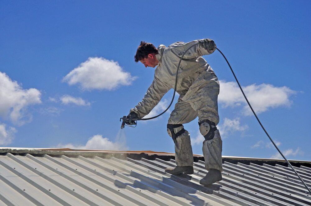 A Man is Spraying Paint on the Roof of a Building — Wagga Roof Repairs In Tumut, NSW