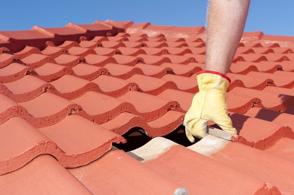 A Person Wearing Yellow Gloves is Working on a Tiled Roof — Wagga Roof Repairs In Tumut, NSW