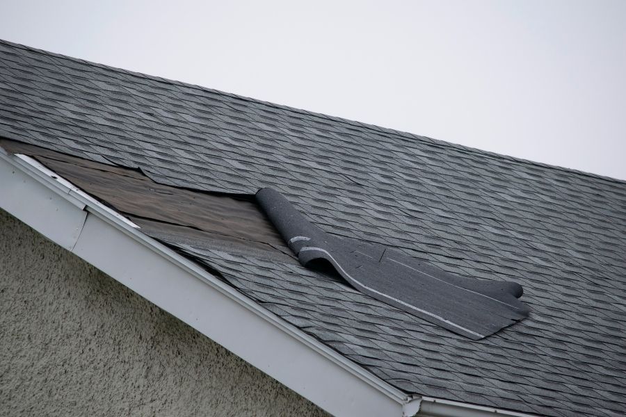 Damaged shingles and exposed roof decking after a storm in Central Texas