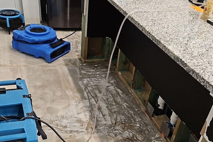 Professional water damage drying setup with industrial air movers and dehumidifiers running in a home after a water leak