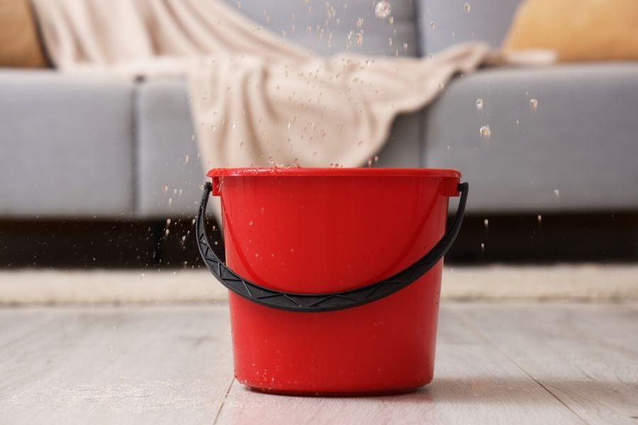Water actively leaking from ceiling into a bucket — a sign that emergency water services are needed immediately