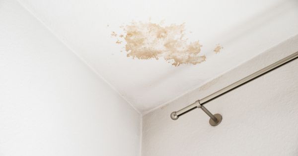 Water-stained white ceiling corner above a curtain rod with a small light fixture