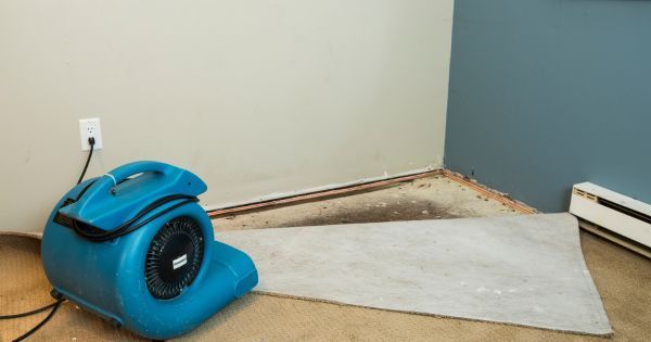 Blue air mover fan drying a wet floor beside a wall in a room