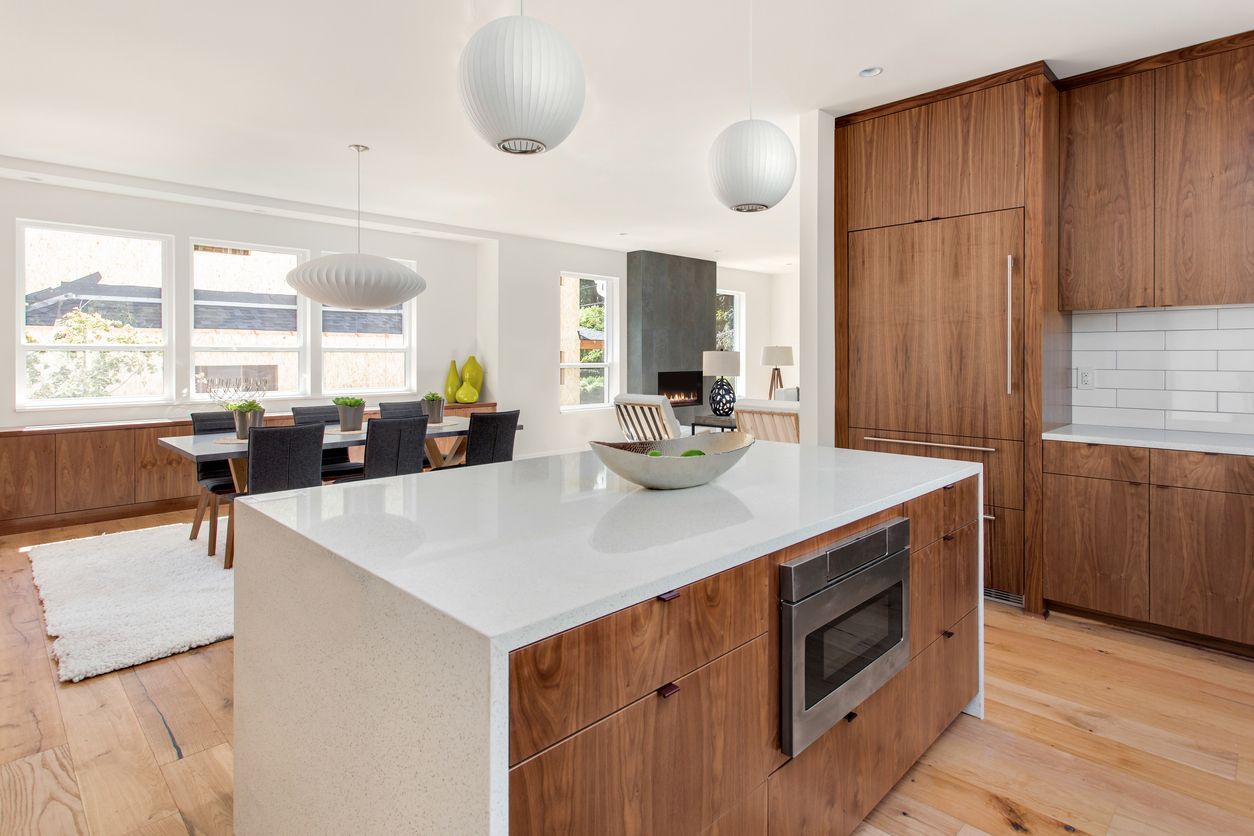 Modern kitchen with wood cabinets, white island, and open dining area with large windows