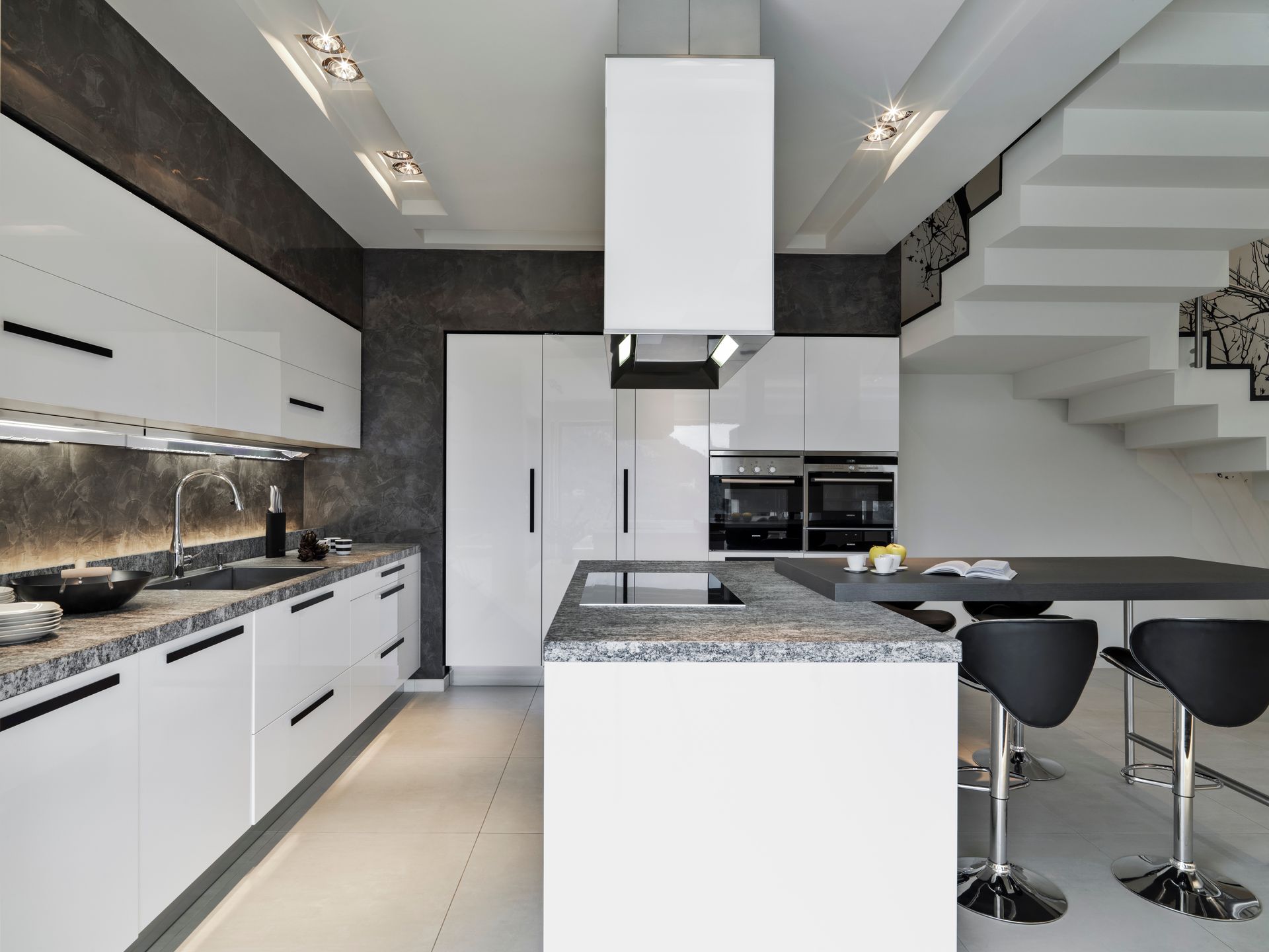 Modern white kitchen with granite countertops, stainless steel appliances, and a breakfast bar.