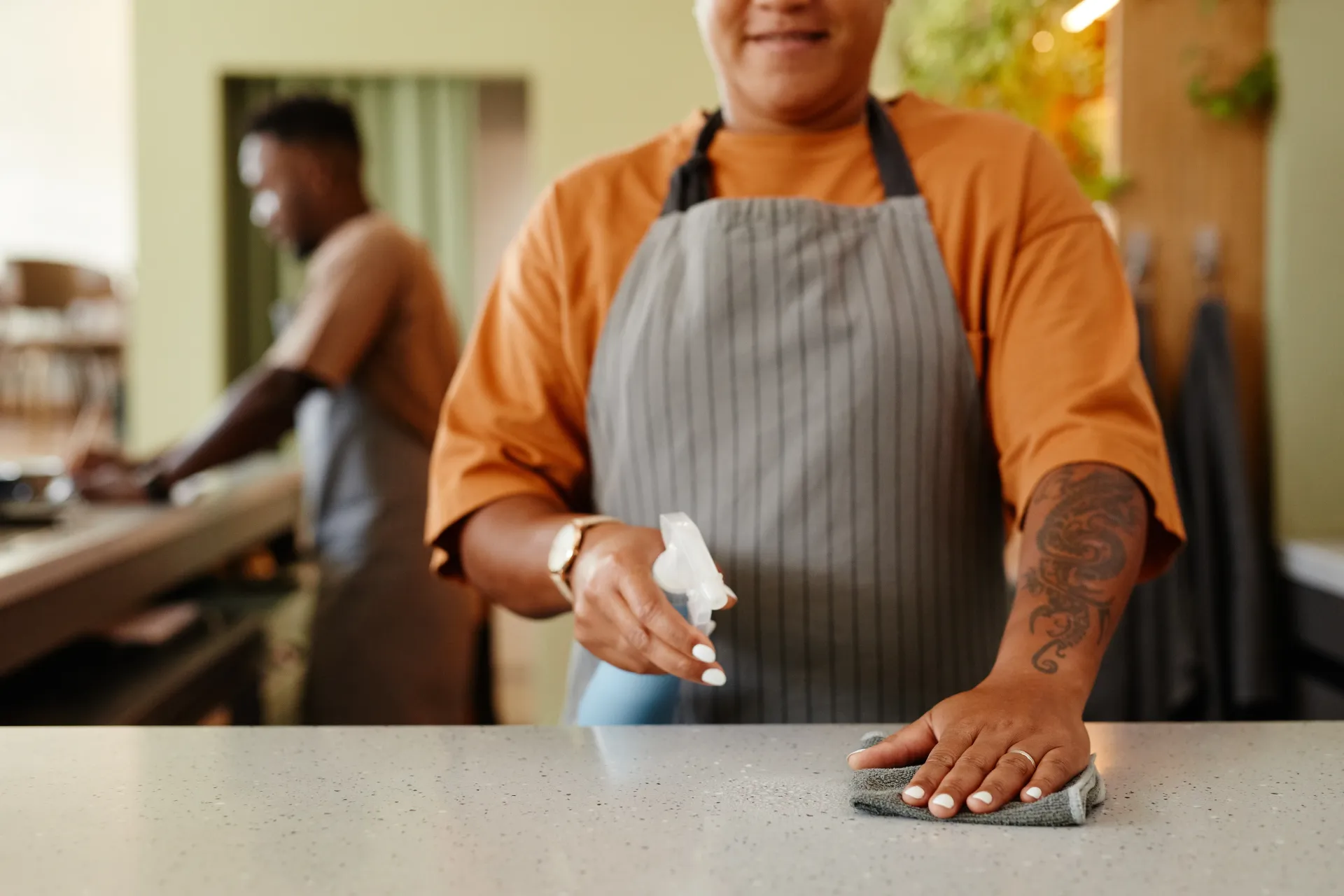 A man in an apron is cleaning a counter in a restaurant.