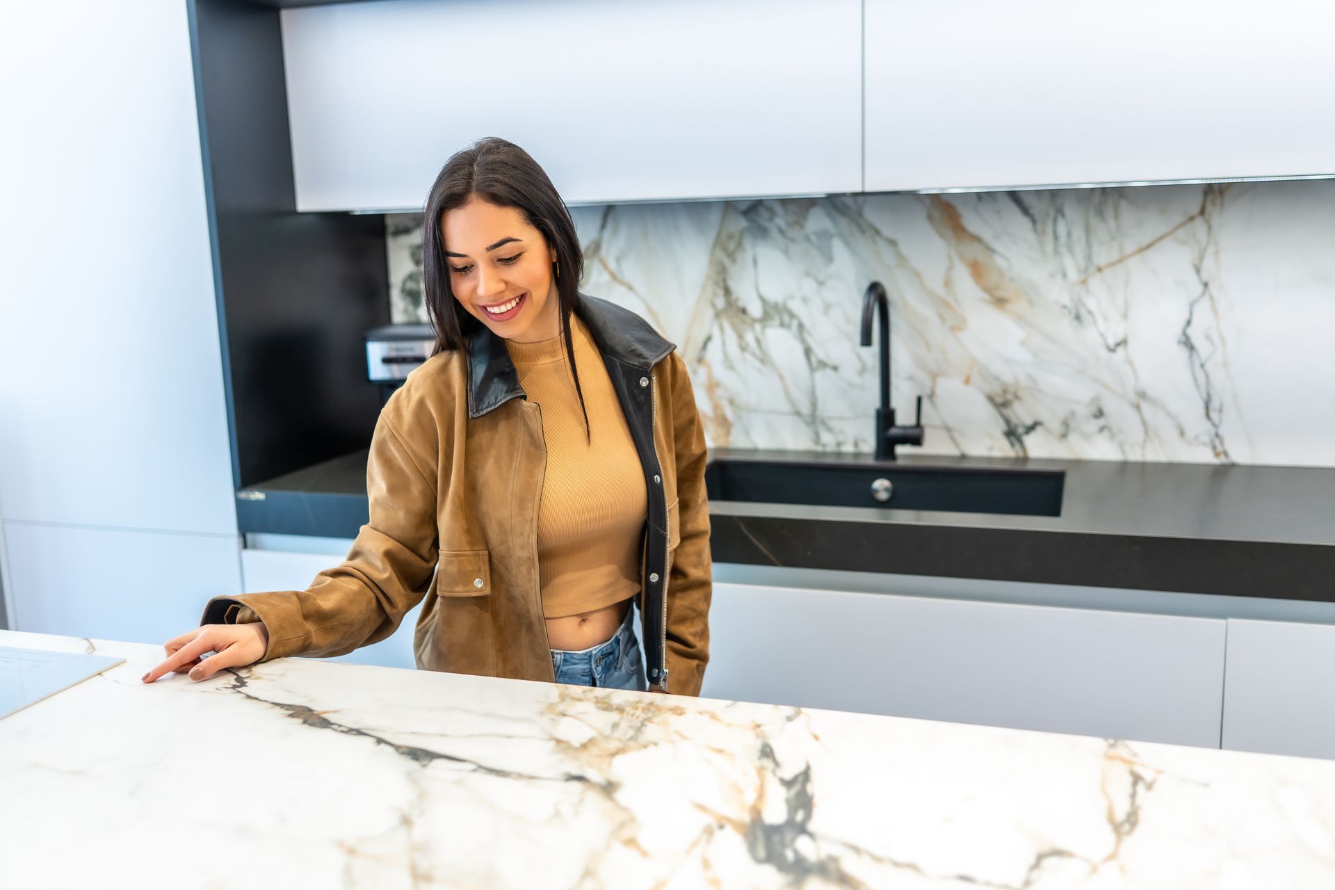 Woman smiles, touches marble countertop in modern kitchen.