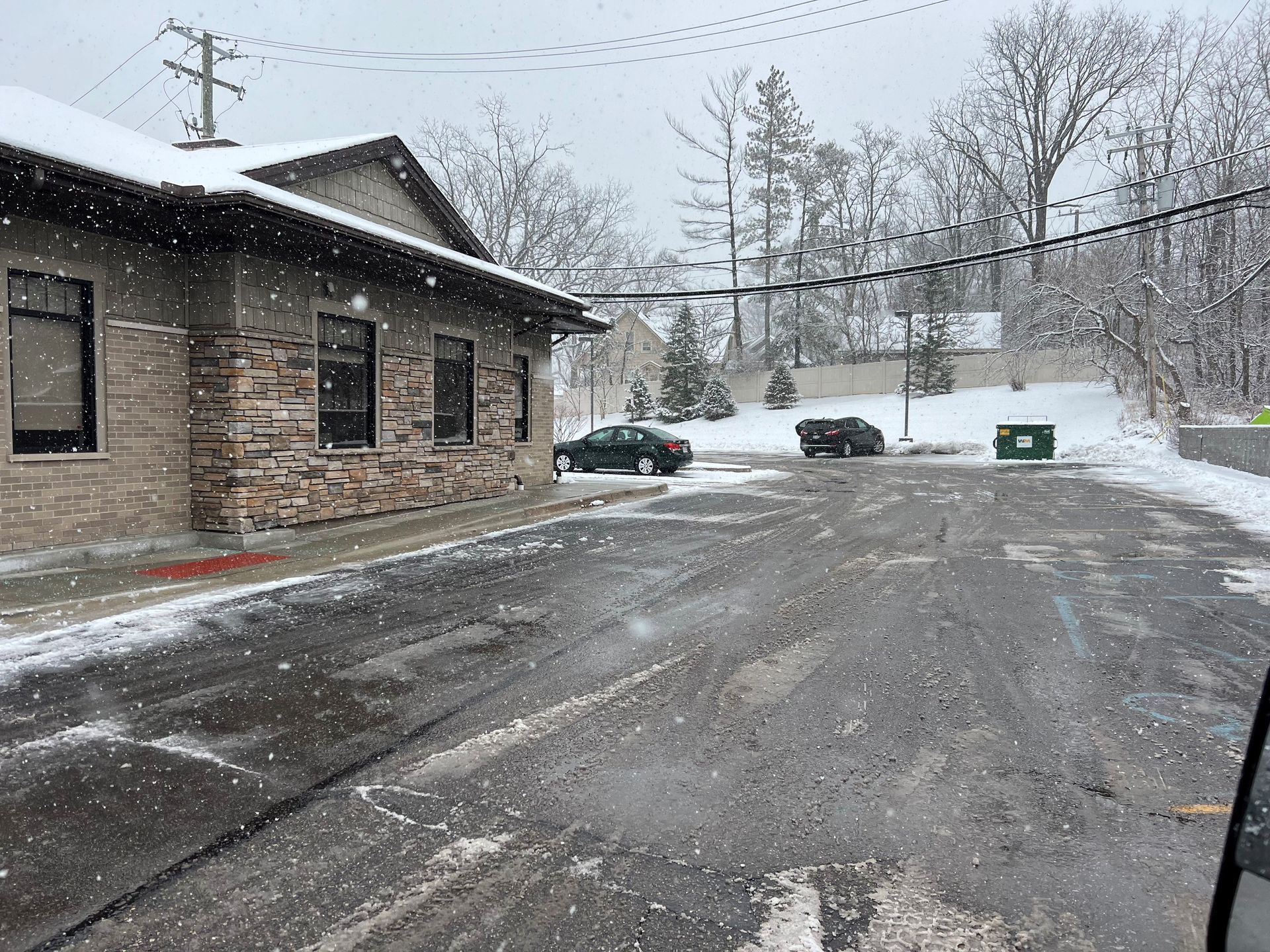 A snowy street with a building in the background and cars parked on the side of the road.