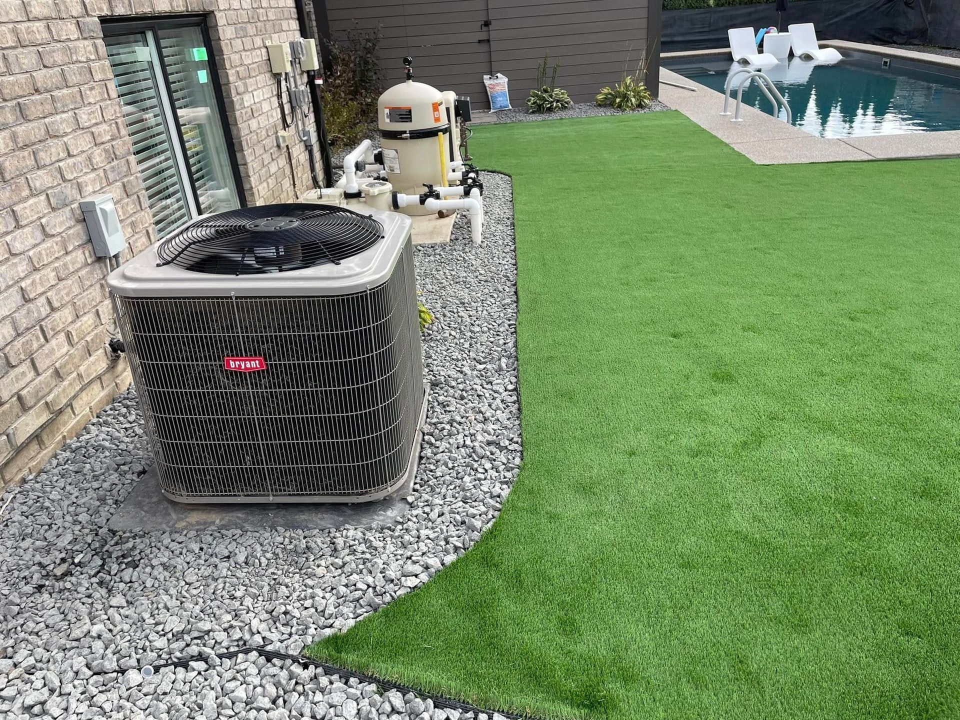 A large air conditioner is sitting on top of a lush green lawn next to a swimming pool.