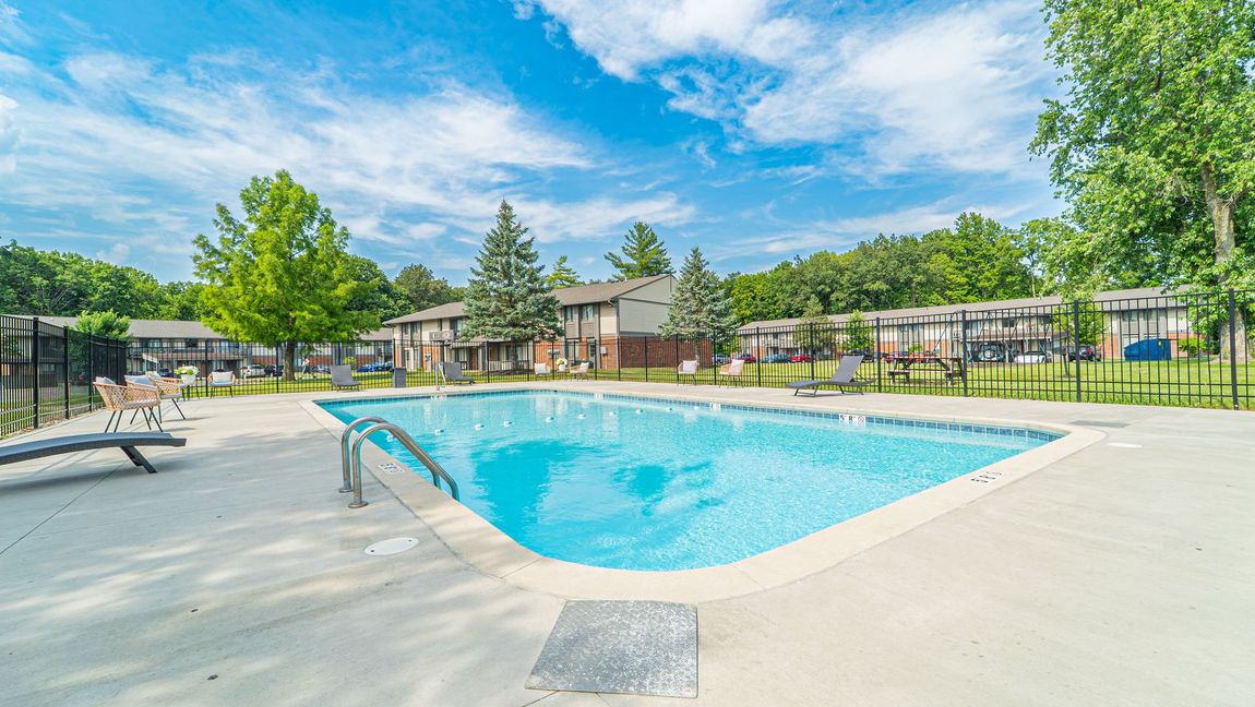 Swimming pool with clear blue water in front of apartment buildings on a sunny day.