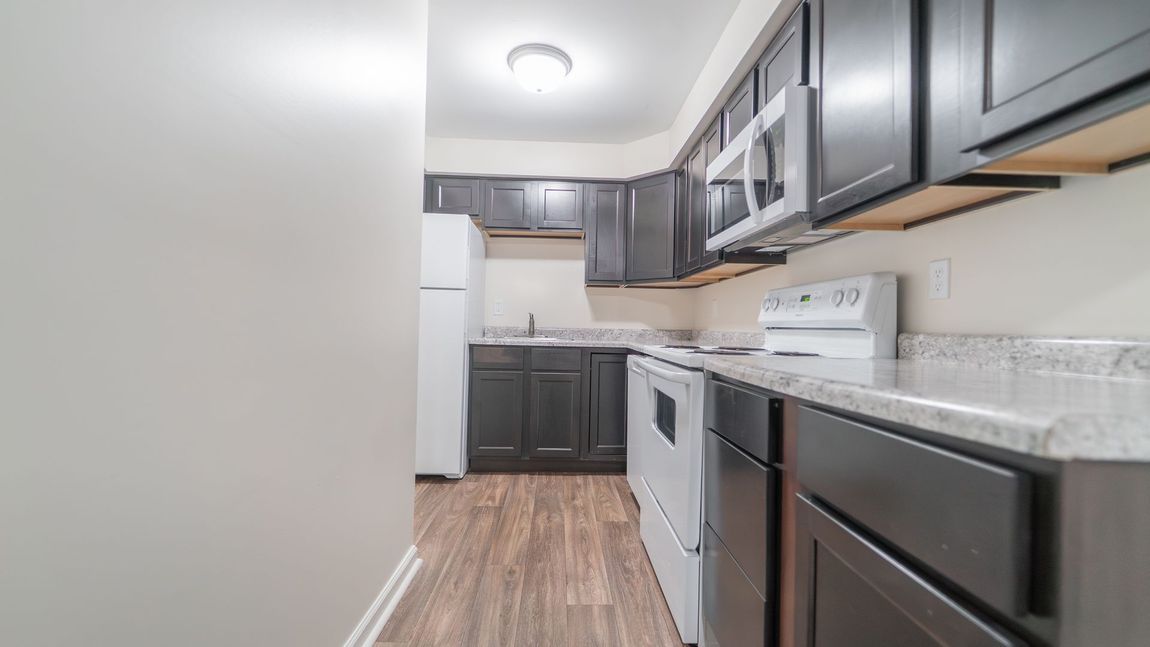 Kitchen with dark cabinets, white appliances, and light countertops.