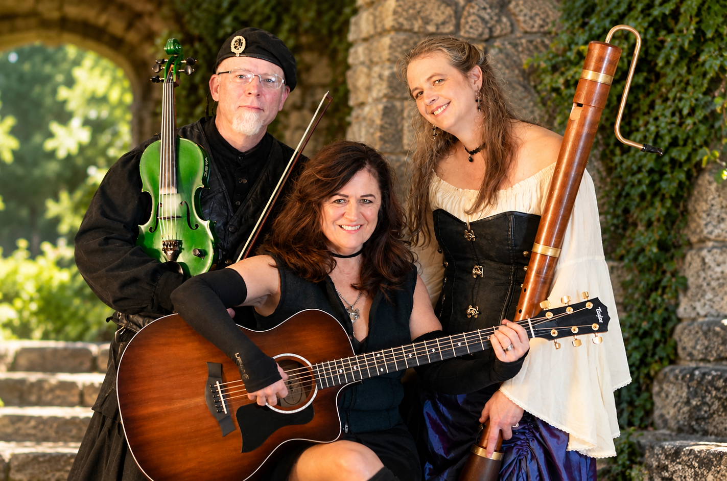 Three musicians pose with guitars and violin in a leafy garden, smiling at the camera.