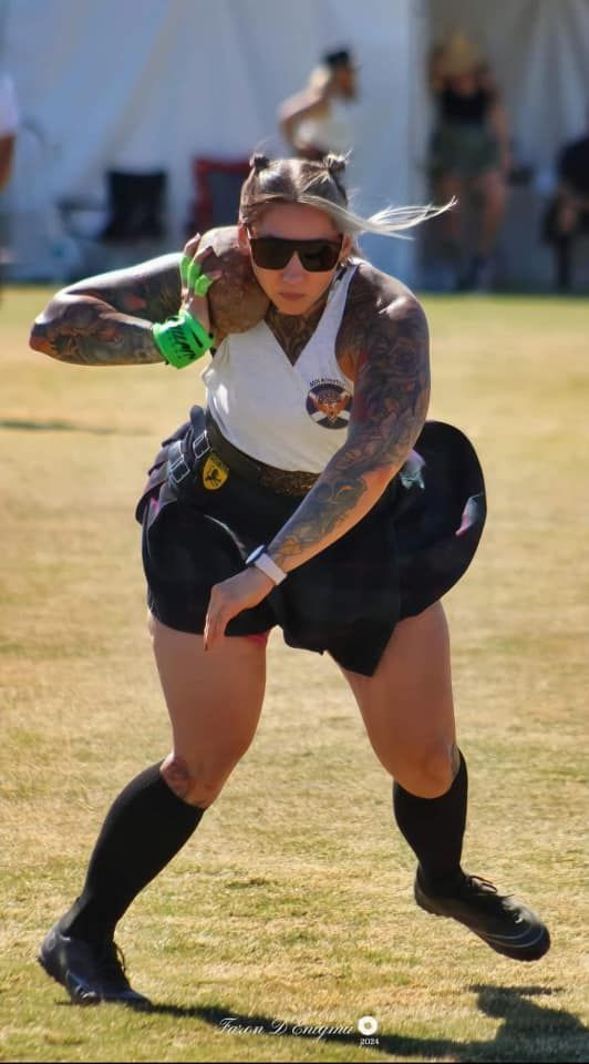 Woman in kilt throws a heavy object in an outdoor sports setting.