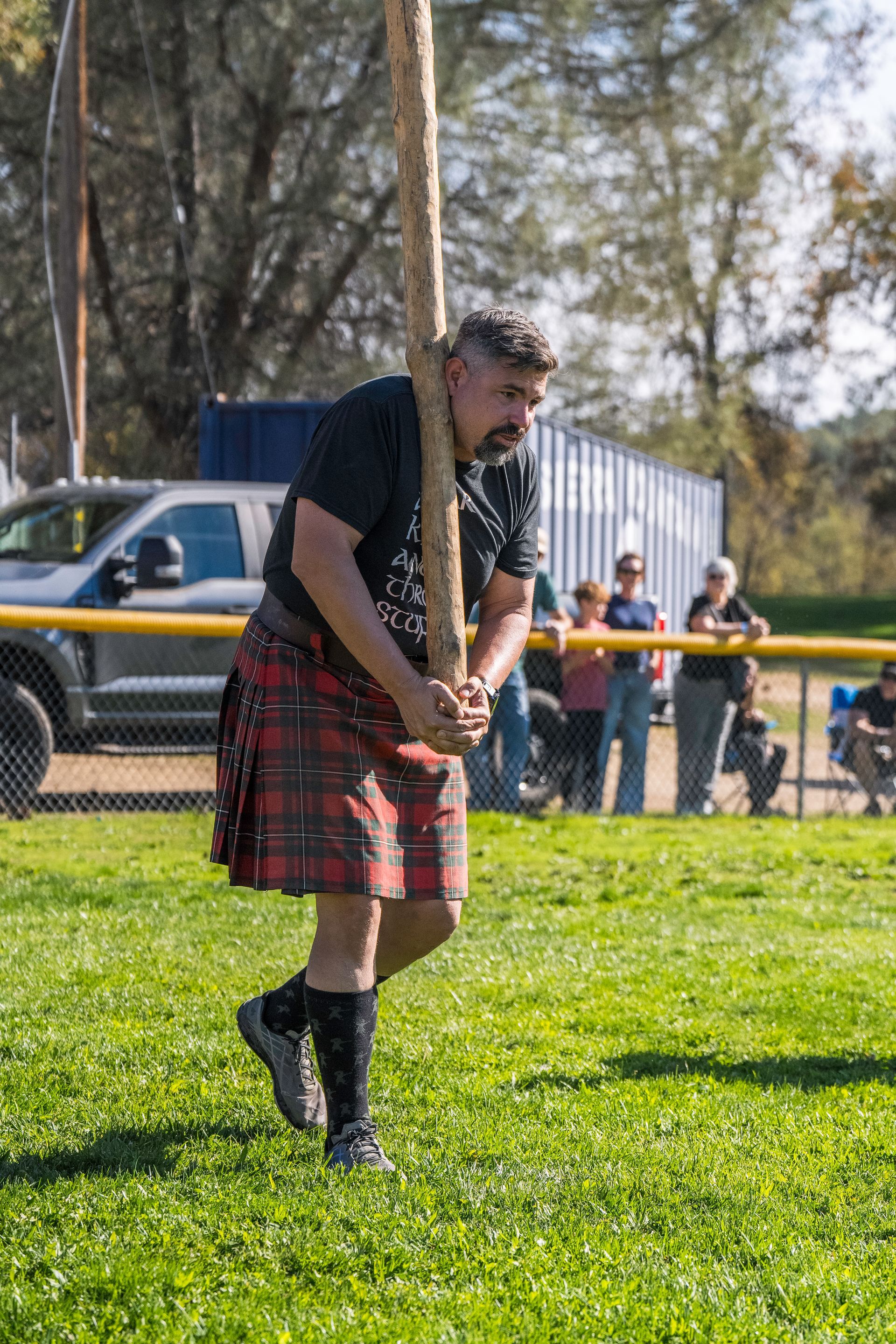 Woman playing a large alphorn in an outdoor arena with a crowd of spectators.