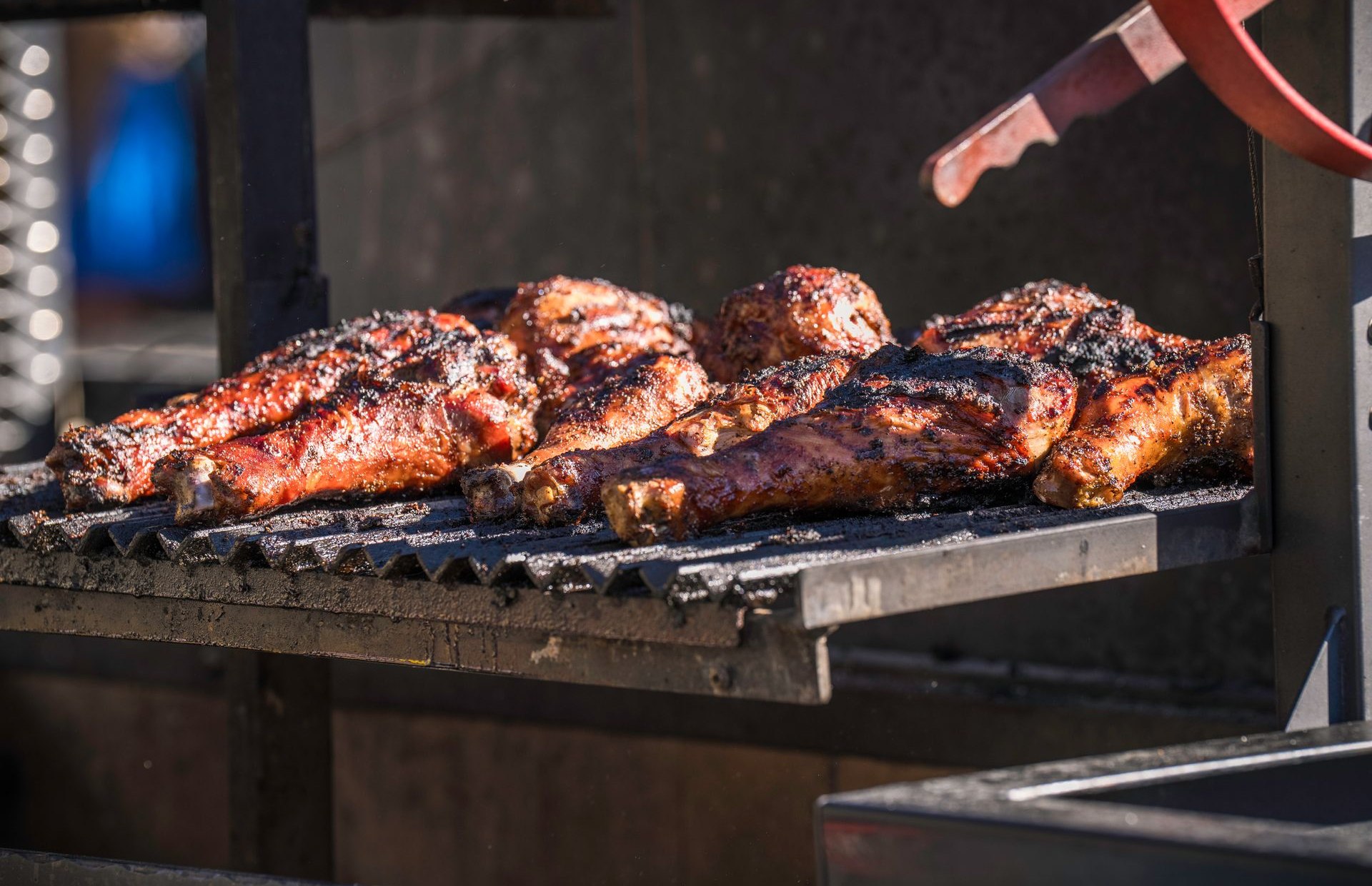 Charred ribs grilling over open flame, with tongs turning the meat on a barbecue pit.
