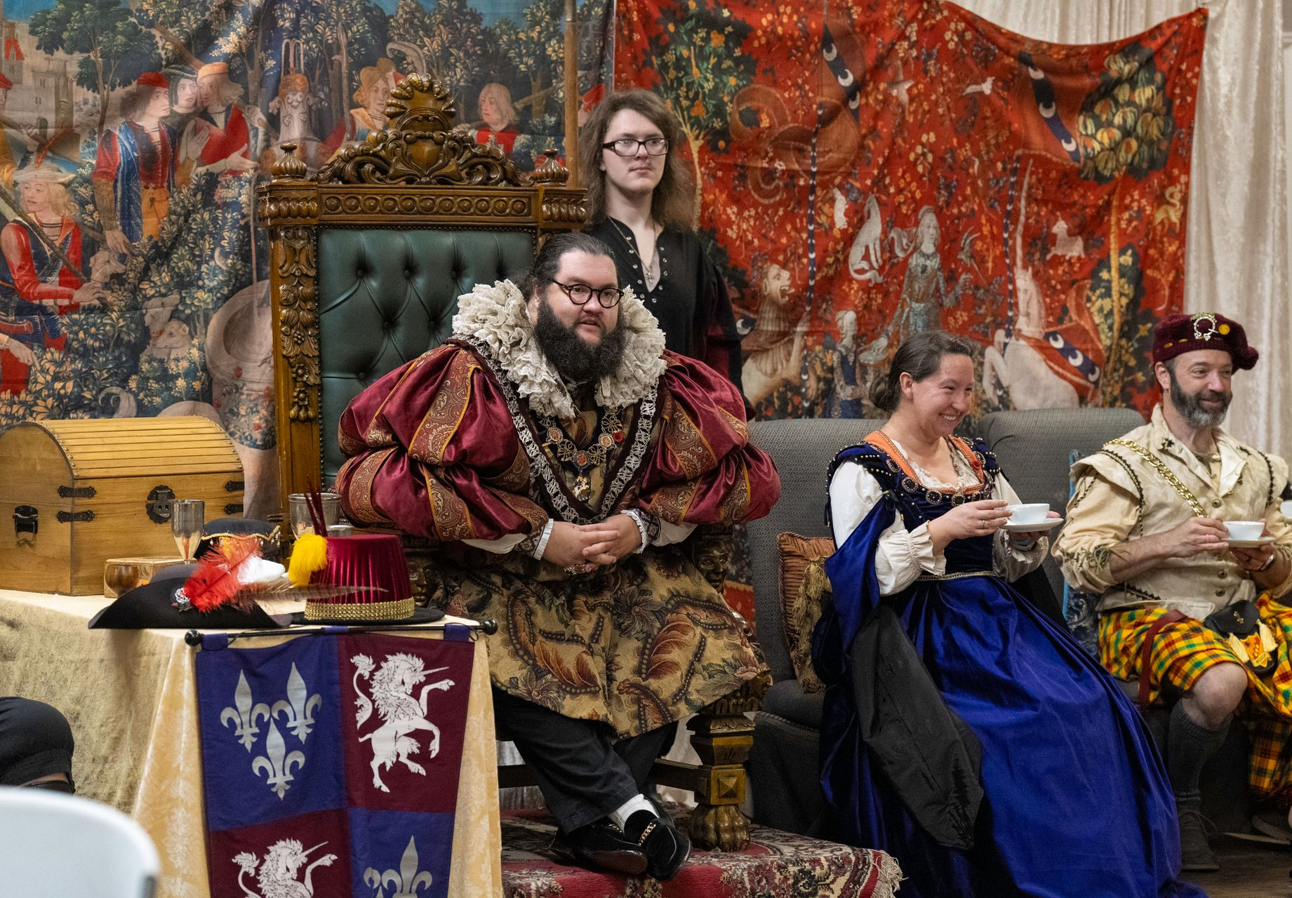 Costumed group seated at a decorated medieval-style banquet table with banners and goblets