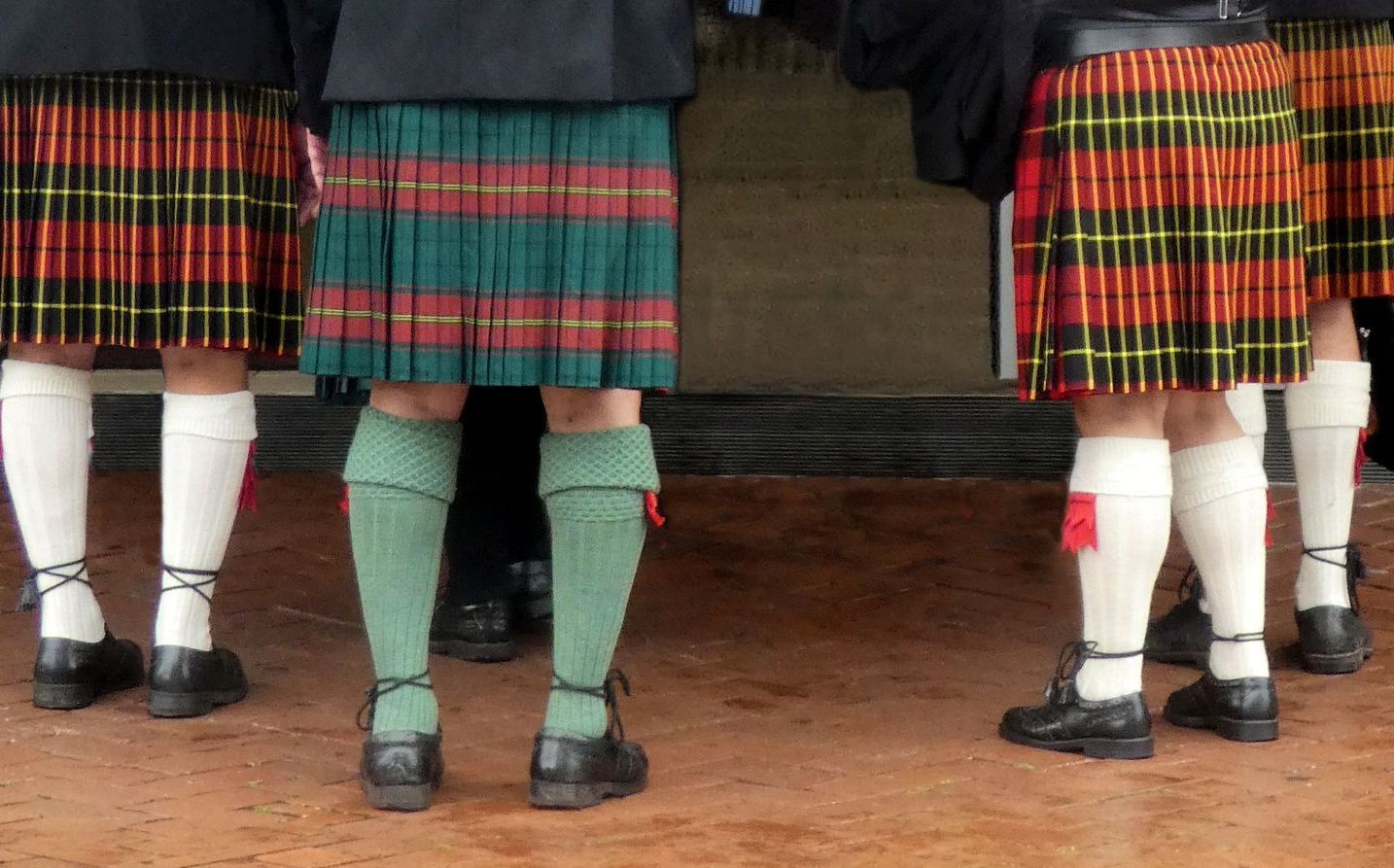 People in kilts and knee socks, gathered outdoors.
