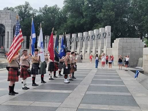 Color guard standing with flags beside a memorial wall in a paved plaza