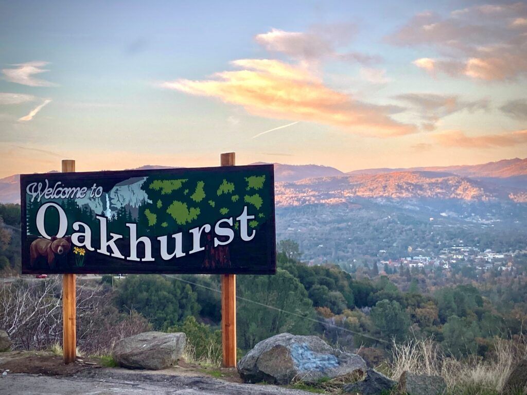 Oakhurst sign overlooking a mountain valley at sunset with clouds and distant city lights