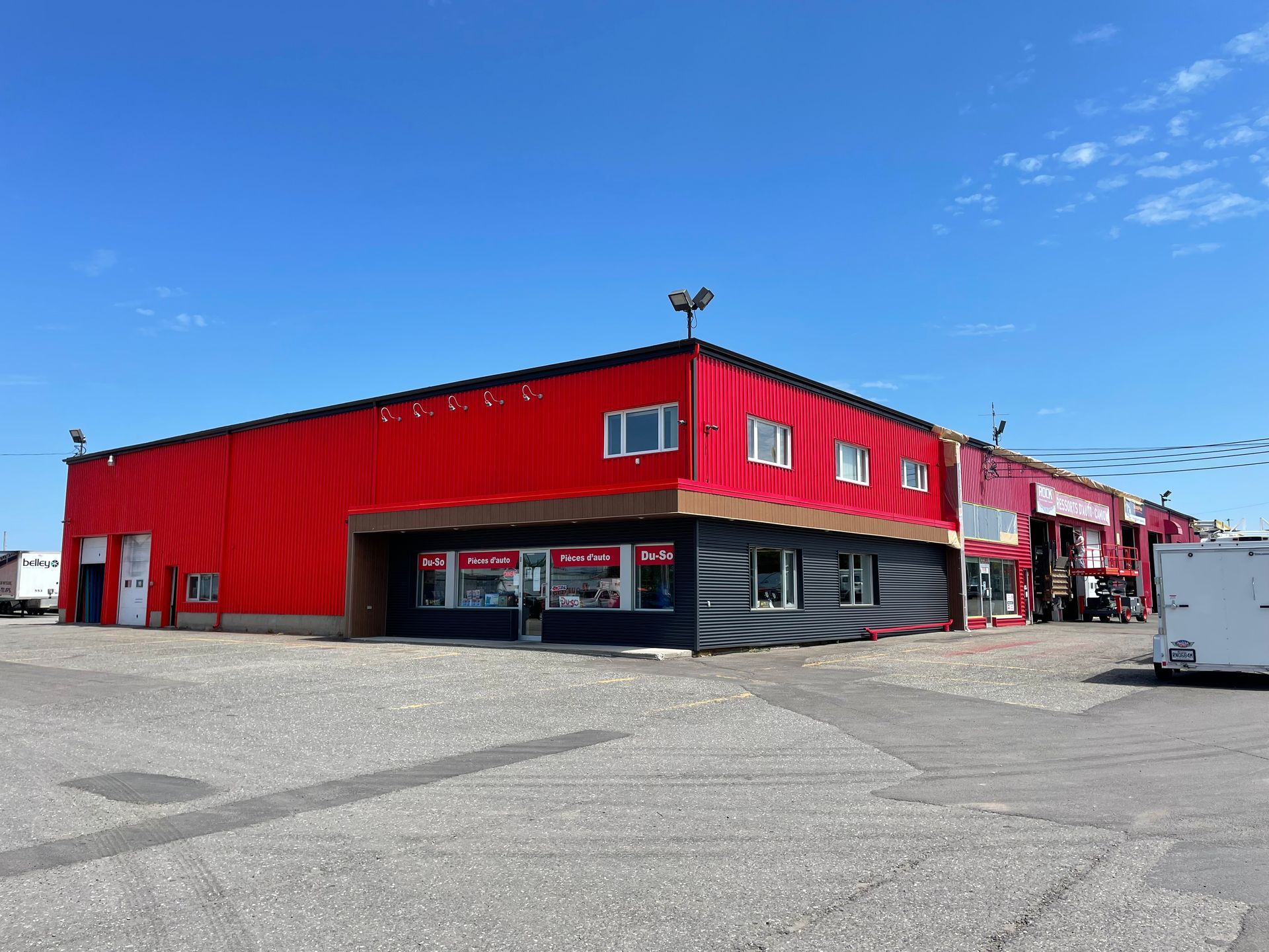 Nacelle élévatrice rouge devant un bâtiment turquoise avec une porte de garage, par temps nuageux.