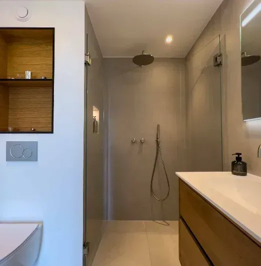 Moderne badeværelse med bruseniche, træhåndvask og indbyggede hylder.