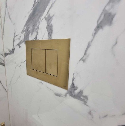 Guldfarvet toiletpanel med dobbeltskyl på hvid marmorvæg.