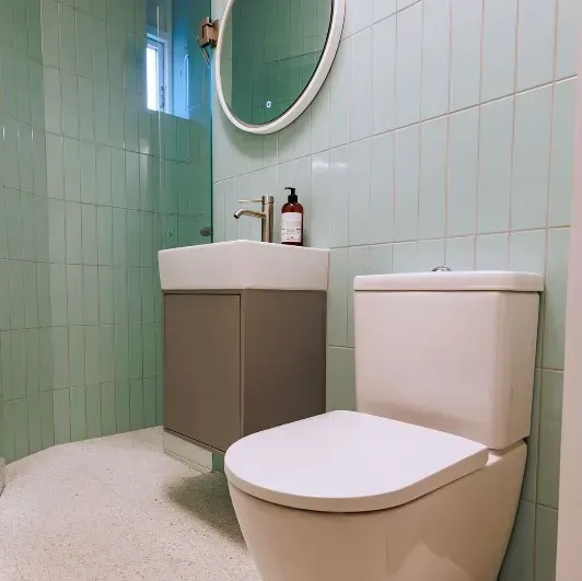 Et lille badeværelse med lyseblå flisebelagte vægge, et hvidt toilet og en håndvask.