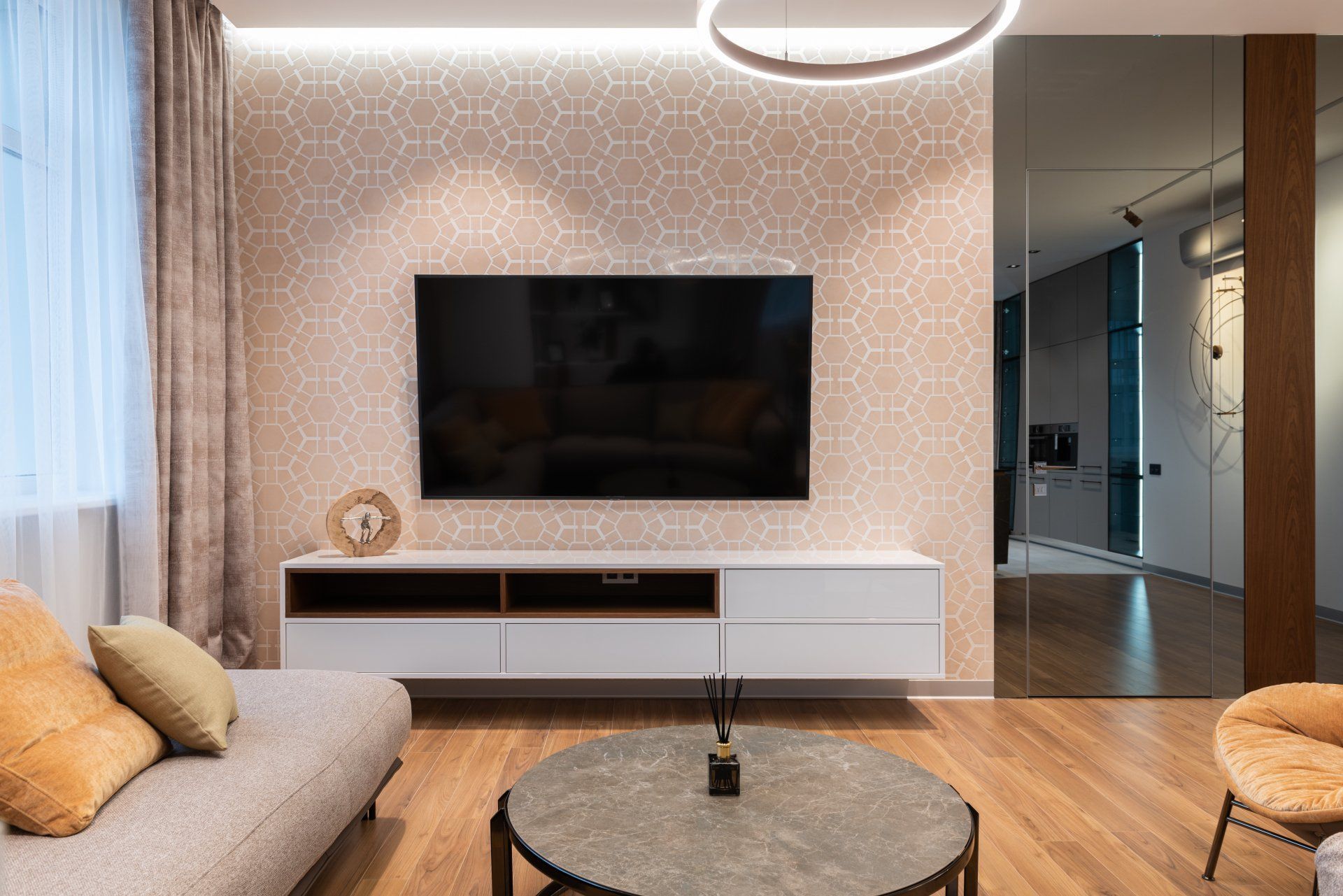 Living room with a floating TV, sofa, coffee table, and patterned wallpaper. Warm colors and modern design.
